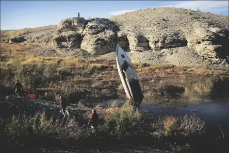  ?? AP PHOTO/JOHN LOCHER ?? People walk by a formerly sunken boat standing upright into the air with its stern buried in the mud along the shoreline of Lake Mead at the Lake Mead National Recreation Area on January 27 near Boulder City, Nevada.