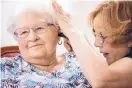  ?? CHRIS MACHIAN/KHN ?? Janie York, right, cleans the hearing aid of Elaine Martin at the SilverRidg­e Assisted Living facility in Gretna, Neb.