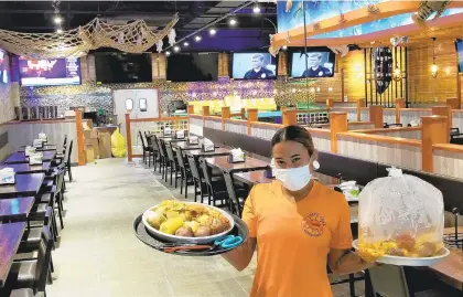  ??  ?? Flaming Crab server Gabriella Pastor holds two daily specials, featuring a lobster tail, half pound of shrimp, half pound of snow crab legs and more, inside the newly opened restaurant’s dining room in Lower Nazareth Township.