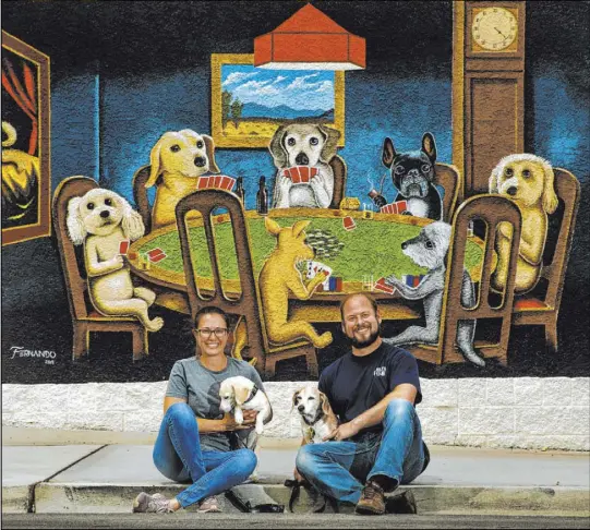  ?? L.E. Baskow Las Vegas Review-Journal @Left_Eye_Images ?? Jill Delozier, holding George, and Adam Pennell, holding Molly, own the Gamblers General Store. The downtown business bears a mural by local artist Fernando Reyes that pays homage to Cassius Marcellus Coolidge’s whimsical Dogs Playing Poker series.