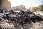  ?? HAIDAR HAMDANI, AFP/GETTY IMAGES ?? Iraqis walk past burntout vehicles Sunday after a twin suicide bombing attack, claimed by the Islamic State in the southern Iraqi city of Samawah.