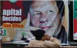  ?? — AP ?? A Pakistani talks on his cell phone while he sits on a bench next to a big poster of Imran Khan, head of Pakistan Tehreek- e- Insaf party, at a market in Islamabad.