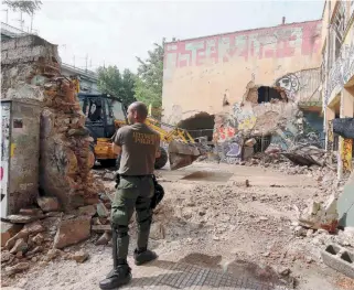  ??  ?? A police officer stands in front of the wreckage of a former orphanage in Ano Toumba, Thessaloni­ki, yesterday, one of several sites that Greek and foreign anarchists have been occupying along with migrants they have hosted.