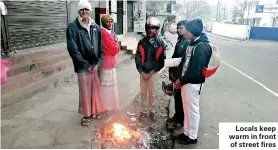  ??  ?? Locals keep warm in front of street fires