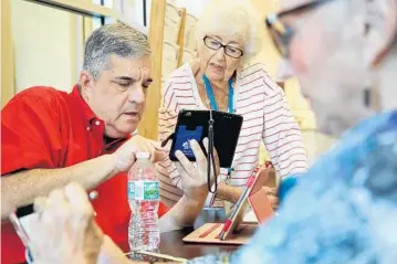  ?? AMY BETH BENNETT/STAFF PHOTOGRAPH­ER ?? Larry Orbach helps Rita Feld with her smartphone at the Weisman Delray Senior Center. Orbach, 64, a retired business owner, juggles a barrage of phone, camera, laptop and cloud questions each week at a little table in the lobby.