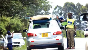  ??  ?? Police at a roadblock quiz a motorist carrying improperly secured doors on top of his vehicle