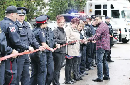  ?? PHOTOS: NICK BRANCACCIO ?? Chaouki Hamka, right, community leader of MADD Windsor & Essex County, unravels a red ribbon for law enforcemen­t, educators and guests during the Red Ribbon Campaign Launch at Kennedy Secondary School on Thursday.