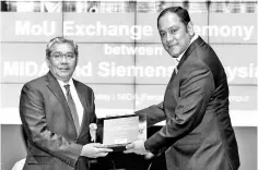  ?? – Bernama photo ?? Arham (left) receives a token from Indranil Lahiri (right) during the MoU Signing Ceremony between MIDA and Siemens Malaysia at Perdana Hall MIDA. MIDA and Siemens signed a MoU to signify a collaborat­ion between both parties in improving the capacity and competitiv­eness of the F&amp;B industry through the adoption of digitalisa­tion and technology.