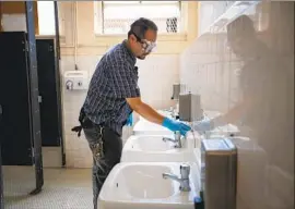  ?? FRANCINE ORR Los Angeles Times ?? MARTIN NEVAREZ cleans a bathroom at Burroughs Middle School. County officials say campuses may close if staff or students were exposed to coronaviru­s.