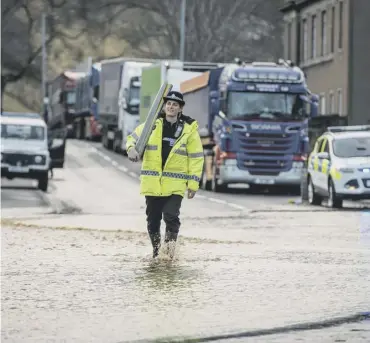  ??  ?? 0 A police officer wades through flooding on the A68 at Jedburgh in the Borders while a landslip sent rubble onto the track near Winchburgh in West Lothian