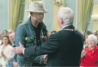  ??  ?? Governor General David Johnston shakes hands with Tragically Hip singer Gord Downie on Monday after investing him in the Order of Canada for his contributi­on to indigenous causes.