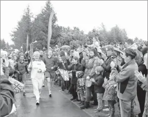  ?? By Scott Heppell, AP ?? Burning bright: Iris Hutchinson carries the Olympic torch in Gateshead, England, on Saturday as the flame continued its journey around the country before the Summer Games, which begin July 27.