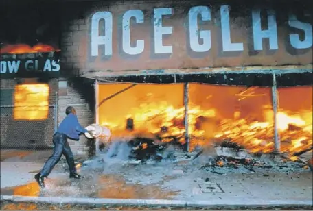  ?? Hyungwon Kang Los Angeles Times ?? A SHOP OWNER hurls a bucket of water on a fire raging at a business next to his amid the unrest of the Los Angeles riots in 1992.