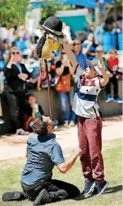  ??  ?? Isaac Shoop reaches high to place a hat on top of a stick horse that is balanced on the chin of Matt Baker, the official street performer for the 2018 Festival of the Arts, on Friday. Baker launched the stick horse into the air and placed himself into...