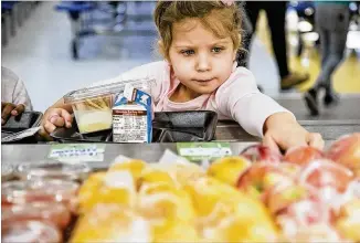  ?? ALYSSA POINTER / ALYSSA.POINTER@AJC.COM ?? Student Mikayla Raidbard reaches for an apple while assembling her food tray during lunch at Heards Ferry Elementary School in Sandy Springs. Healthful entree options including bento boxes with hummus and fresh vegetables are popular with the students.