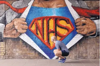  ?? MATT DUNHAM/ASSOCIATED PRESS ?? On Sunday, a jogger stops to tie his shoe in front of a new mural with a National Health Service Superman motif. Street artist Lionel Stanhope painted the mural, which is in the Waterloo area of London.