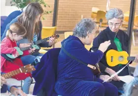  ??  ?? Charlotte Graham, 5, the youngest participan­t in the ukulele jam session, plays alongside her mother, Jen, while K.C. Cotkin, second from right, discusses a piece of music with Su Hudson.