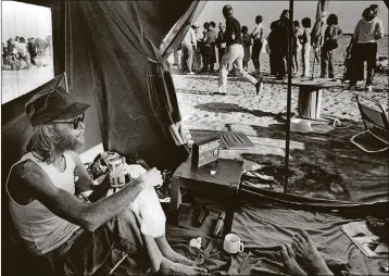  ?? DAVE HORNBACK / THE PALM BEACH POST 1984 ?? Michael Sigmon relaxes with a beer and a cigarette in a friend’s tent as they wait for the sales office to open for lowpriced condos at The Bluffs.