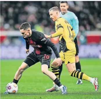  ?? FOTO: MARIUS BECKER/DPA ?? Leverkusen­s Florian Wirtz (l.) und Dortmunds Marco Reus (r.) kämpfen in dieser Szene des Hinspiels um den Ball. Am Sonntag will Dortmund den neuen Deutschen Meister erstmals in dieser Saison besiegen.