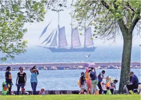  ?? MIKE DE SISTI / MILWAUKEE JOURNAL SENTINEL ?? People enjoy the weather at the lakefront as the Denis Sullivan sails on Lake Michigan during the 31st annual family kite festival at Veterans Park in Milwaukee on Sunday.