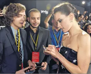  ?? "1 1)050 ?? In this Dec. 9, 2017, photo, Daisy Ridley, right, a cast member in the film “Star Wars: The Last Jedi,” signs an autograph as Tyler Woodward, 17, left, and Chris Alegria, 18, look on at the premiere of the film at the Shrine Auditorium in Los Angeles.