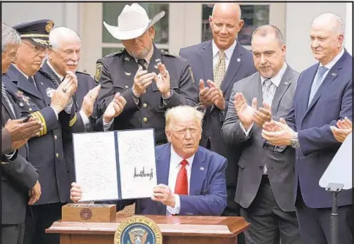  ?? /ALEX WONG/GETTY IMAGES ?? Surrounded by members of law enforcemen­t, President Trump holds up an executive order he signed on “Safe Policing for Safe Communitie­s” in the White House Rose Garden on Tuesday.