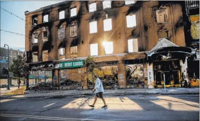  ?? Elizabeth Flores The Associated Press ?? A man walks past a damaged building Sunday in Minneapoli­s following overnight protests over the death of George Floyd. Protests were held throughout the country over the death of Floyd, a black man who died in police custody on May 25.