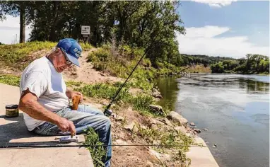  ?? Chris Machian/Associated Press ?? Bob Ridge baits a fishhook at the Elkhorn River on Thursday in Omaha, Neb. Health officials say a child died likely from a rare infection caused by a brain-eating amoeba after swimming in the river last Sunday.