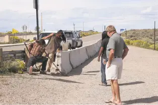  ?? JESSE MOYA/THE TAOS NEWS ?? Tourists watch as a crew of bridge vendors moves a barricade to create a walkway for people to access their goods. Vendors arrived Thursday morning to hundreds of new concrete barriers placed in the area where they normally sell merchandis­e.