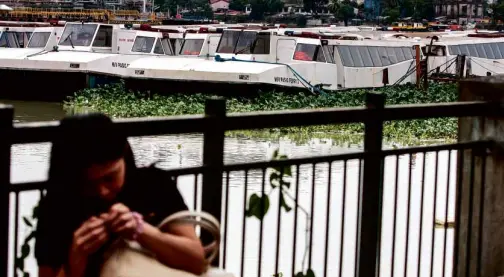  ?? LEOM. SABANGAN II ?? A STUDENT whiles away the time by the Pasig, with underused ferryboats in the background.