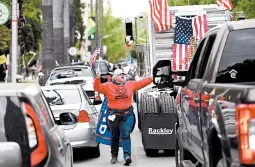  ?? JOSH EDELSON/GETTY-AFP ?? A woman wearing a Trump flag walks through gridlocked traffic Monday as hundreds of people protested California’s shelter-in-place rules at the state Capitol in Sacramento.