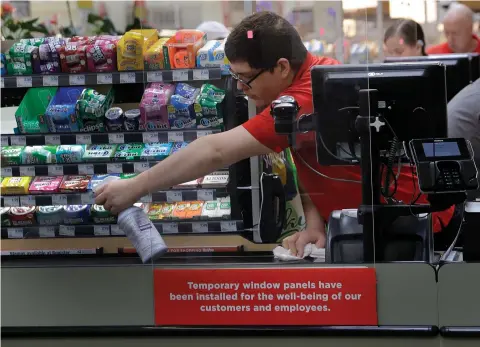  ?? ASSOCIATED PRESS ?? In this March 26, 2020, file photo, Garrett Ward sprays disinfecta­nt on a conveyor belt between checking out shoppers behind a plexiglass panel at a Hy-vee grocery store in Overland Park, Kan. From South Africa to Italy to the U.S., grocery workers — many in lowwage jobs — are manning the front lines amid worldwide lockdowns, their work deemed essential to keep food and critical goods flowing.