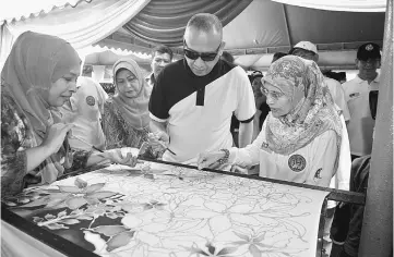  ??  ?? Nazri trying his hand at batik painting after opening the culture and arts community programme. — Bernama photo