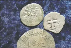  ??  ?? A 17th century Arabian silver coin (top) rests near an Oak Tree Shilling minted in 1652 by the Massachuse­tts Bay Colony (below) and a Spanish half real coin from 1727 on a table.