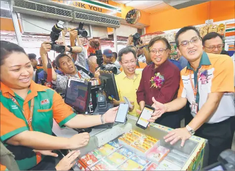  ?? — Photo by Muhammad Rais Sanusi ?? Abang Johari, flanked by Dr Sim (front, third right) and Chai, tries his hands at transactin­g via Sarawak Pay app at the KK Store.