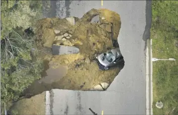  ?? Myung J. Chun Los Angeles Times ?? A VEHICLE is trapped in a sinkhole in Chatsworth on Tuesday. The ferocity of recent storms has caught California­ns off guard. The death toll from them is higher than that of the last two wildfire seasons combined.