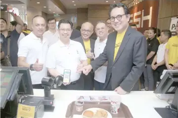  ??  ?? Kamaruzzam­an (second left) and Abdul Farid (right) demonstrat­e the ease of payment at KFC counter using the new capability of QRPay.