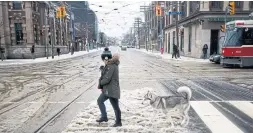  ?? COLE BURSTON/THE CANADIAN PRESS ?? A woman crosses the street with a dog in her jacket and another in tow. Snow and cold in mid-April are more common than you think, Judith Timson writes.
