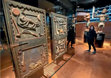  ?? AP ?? A visitor looks at a door from the king’s palace and wooden royal statues from the 19th-century Dahomey kingdom, today’s Benin, at the Quai Branly museum in Paris. French President Emmanuel Macron has commission­ed a report on how former colonisers can return African art to Africa.