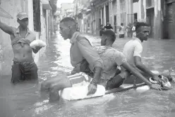  ?? Associated Press photos ?? n LEFT: Residents float down a flooded street in Havana atop a large piece of plastic foam Sunday. There were no immediate reports of deaths in Cuba, a country that prides itself on its disaster preparedne­ss, but authoritie­s were trying to restore...