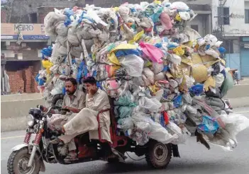  ?? — AFP ?? Men drive a three-wheeler loaded with used plastic bags in Lahore.