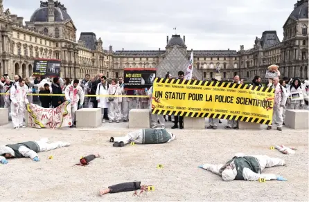  ?? Picture: AFP ?? The French forensic police yesterday hold a banner reading ‘A status for forensic police’ at a fake crime scene, with the Louvre in background, during a demonstrat­ion to demand considerat­ion over their dangerous work in Paris. It is part of a nationwide multi-sector strike against the French government’s pensions overhaul. The status difference within the police between the armed agents and those of the technical and scientific police exasperate the latter.