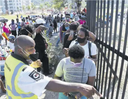  ?? (Photo: Naphtali Junior) ?? A Guardsman security guard instructs people waiting outside the National Stadium car park to collect compassion­ate grants earlier this year.