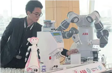  ??  ?? A man shows how a robot works as it prepares medicine for patients. Siriraj Hospital and its alliances have developed robots to work in the hospital’s pharmacies. The machines are aimed at improving patient safety and limiting dispensary mistakes.