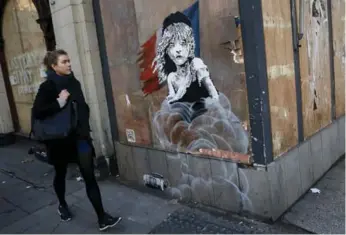  ?? STEFAN WERMUTH/REUTERS ?? A woman walks past the new graffiti mural attributed to Banksy. It appeared Saturday night in London, England.