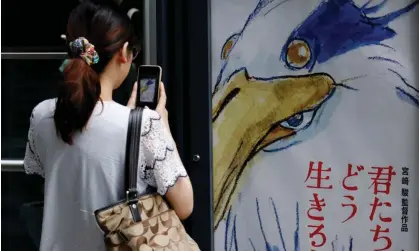  ?? Photograph: Kim Kyung-Hoon/Reuters ?? A woman takes a picture of a movie poster for Hayao Miyazaki's film How Do You Live? outside a movie theatre in Tokyo, Japan, on Friday.