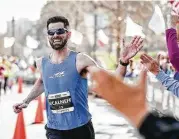  ??  ?? Calum Neff, of Katy, slaps hands with spectators as he approaches the finish line in first place for men’s overall during the 6th annual The Woodlands Marathon on Saturday.