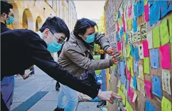  ?? Photog r aphs by Patrick Hamilton AFP/ Getty I mages ?? SUPPORTERS of the Hong Kong pro- democracy protests, wearing masks to conceal their identities, post sticky notes on a “Lennon Wall” in August 2019 at the University of Queensland in Brisbane, Australia.