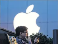  ?? AP PHOTO/NG HAN GUAN ?? In this May 13, 2016, file photo, a man uses his mobile phone near an Apple store in Beijing. This week, Apple announced it will open a data center in mainland China with ties to the country’s government, raising concerns about the security of iCloud...