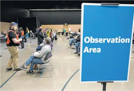  ?? TED S. WARREN/AP ?? A worker, left, checks in with people sitting in an observatio­n area after they were given the Pfizer vaccine on Jan. 24 in Seattle. After getting the shot, patients were required to stay on site for at least 15 minutes to be observed for any adverse reactions.